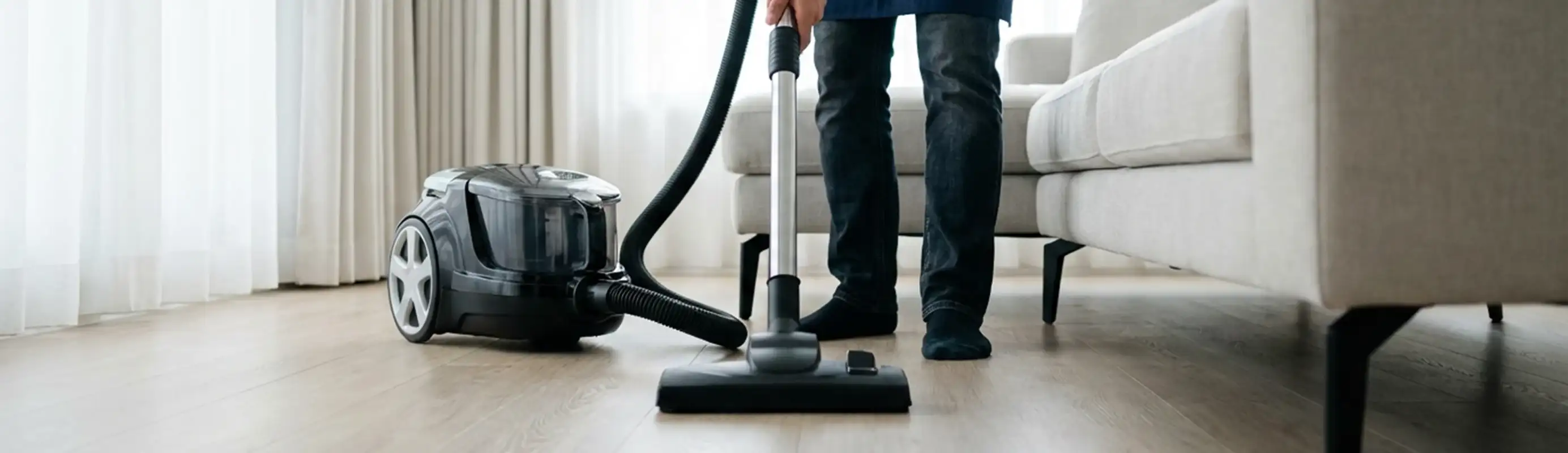 Professional house cleaner vacuuming a living room floor with a canister vacuum cleaner, Hialeah, FL.