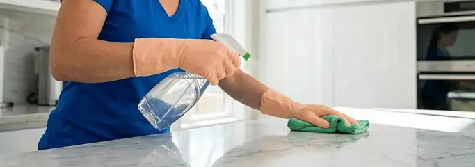 Maid service worker spraying and wiping a kitchen countertop with a microfiber cloth for sanitizing, Hialeah, FL.