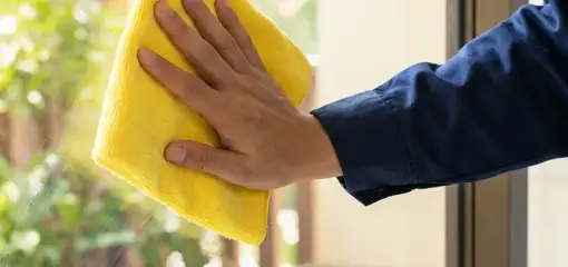 House cleaner wiping a glass window with a yellow microfiber cloth for streak-free cleaning, Hialeah, FL.